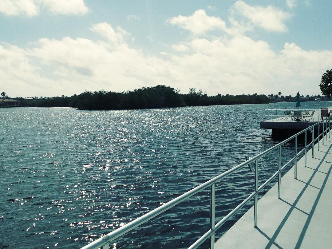 A metal railing lines a concrete walkway overlooking a sunlit bay with a distant island — 880 W Horizons # 111, Boynton Beach FL 33435, BOYNTON BEACH, FL
