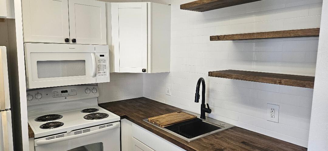 A kitchen features white cabinets, a white stove, dark wood countertops, and open wooden shelving — 880 W Horizons # 111, Boynton Beach FL 33435, BOYNTON BEACH, FL