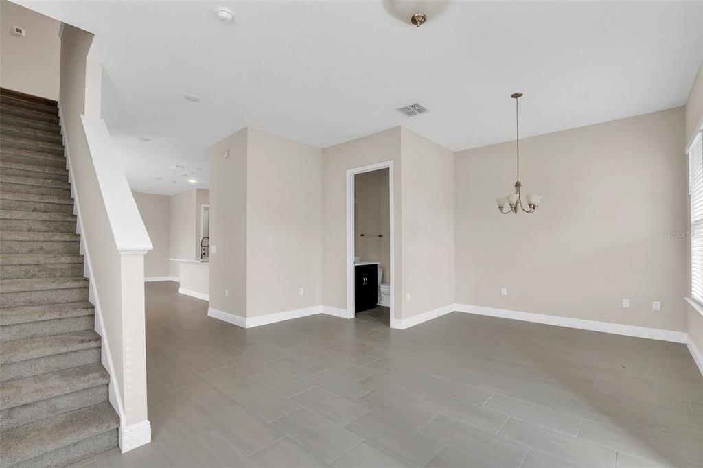 An open-concept dining area features gray tile flooring, a staircase, and a doorway to a bathroom — 2953 VOYAGER AVENUE, ST CLOUD, FL