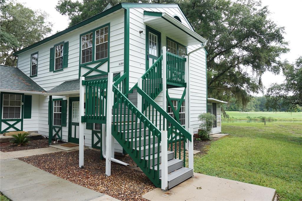 A two-story white building with green trim and an exterior staircase leading to the second floor — 7945 MIDWAY DRIVE TERRACE UNIT H201, OCALA, FL