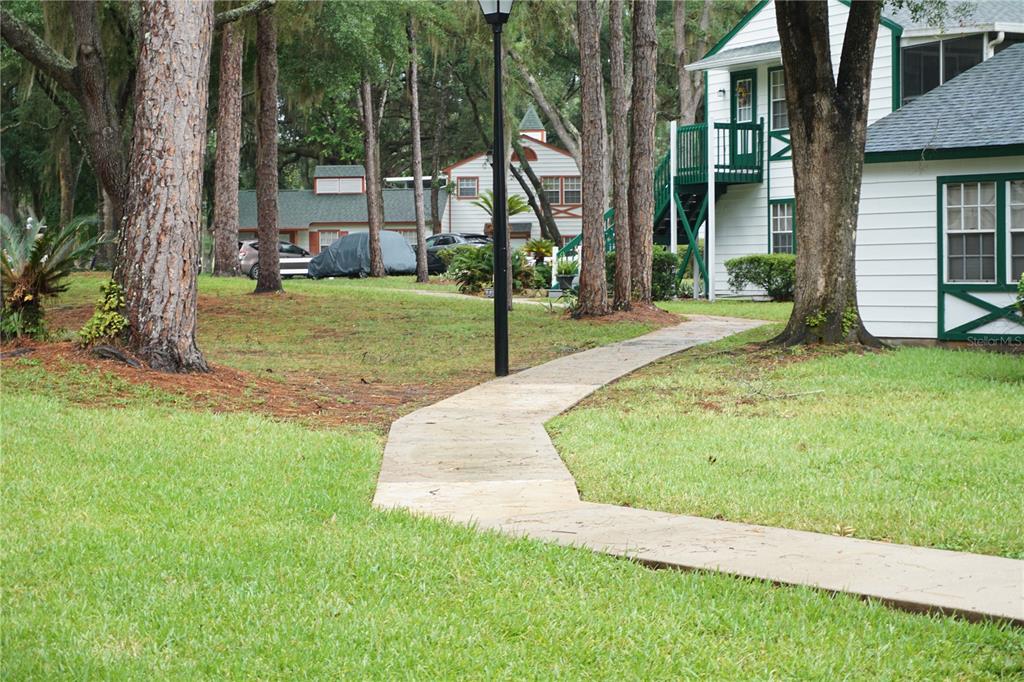 A concrete walkway winds through a grassy yard between trees and white residential buildings — 7945 MIDWAY DRIVE TERRACE UNIT H201, OCALA, FL