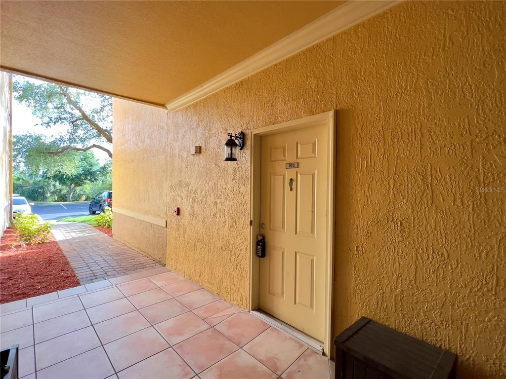 A covered entryway with a tiled floor leads to a beige door labeled 102 — 4309 BAYSIDE VILLAGE DRIVE UNIT 102, TAMPA, FL