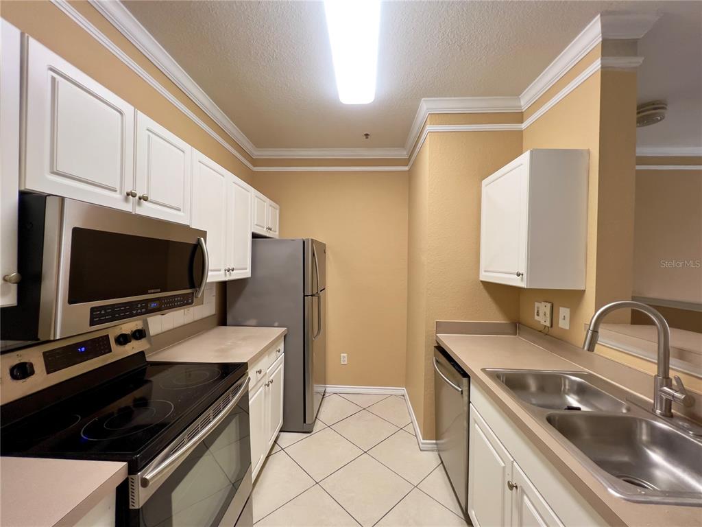 A kitchen features white cabinets, stainless steel appliances, tan countertops, and light-colored tile flooring — 4309 BAYSIDE VILLAGE DRIVE UNIT 102, TAMPA, FL