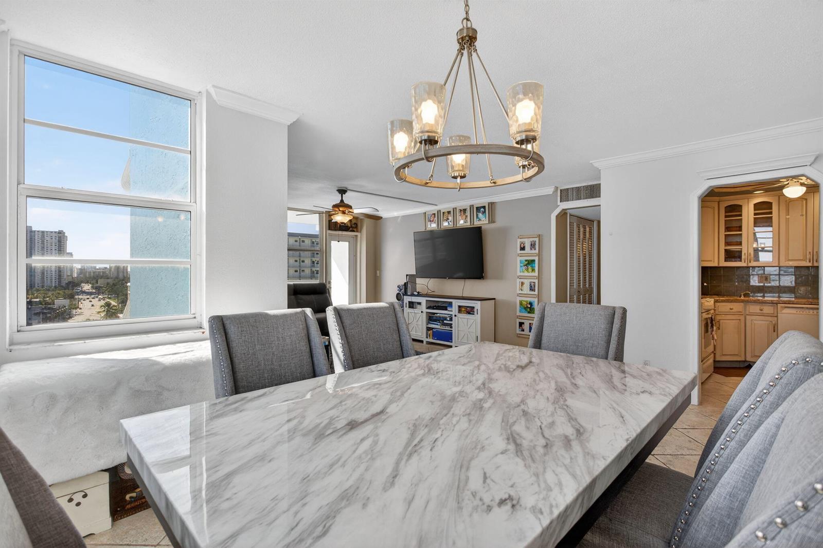 A dining area features a marble-topped table, gray upholstered chairs, and a modern chandelier — 301 N Ocean Boulevard # 1006, Pompano Beach FL 33062, POMPANO BEACH, FL