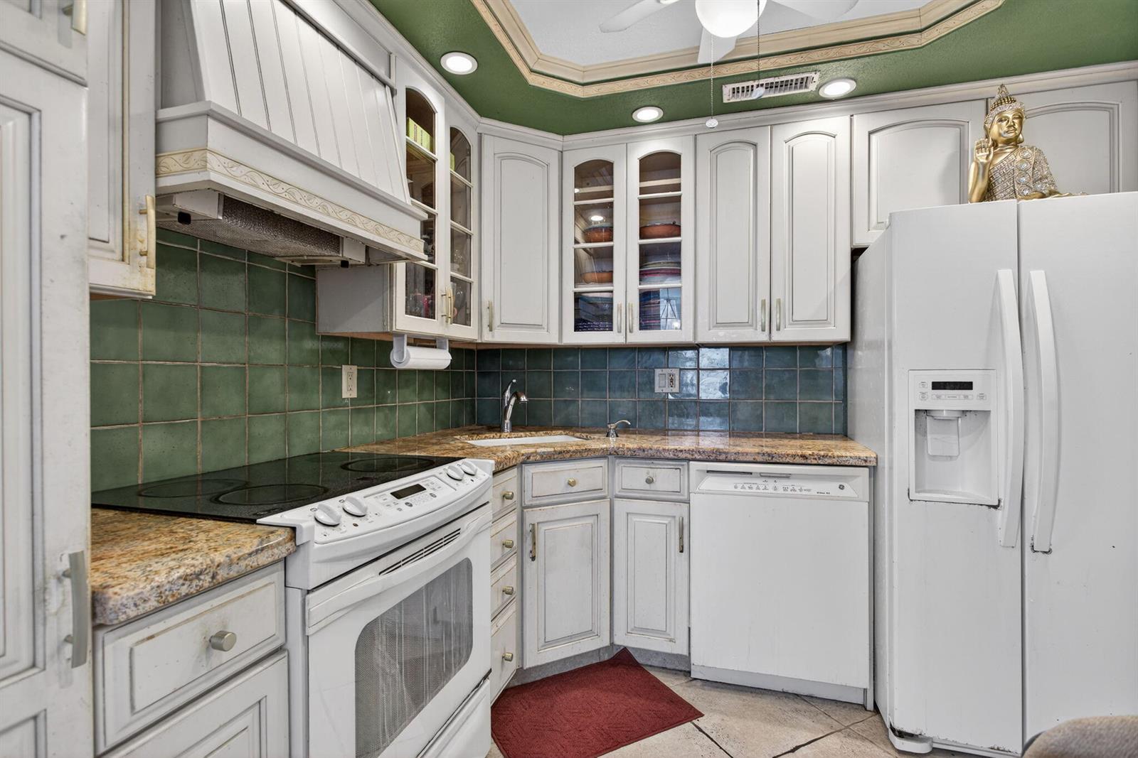 A kitchen features white cabinets, green tile backsplash, granite countertops, and a white refrigerator — 301 N Ocean Boulevard # 1006, Pompano Beach FL 33062, POMPANO BEACH, FL