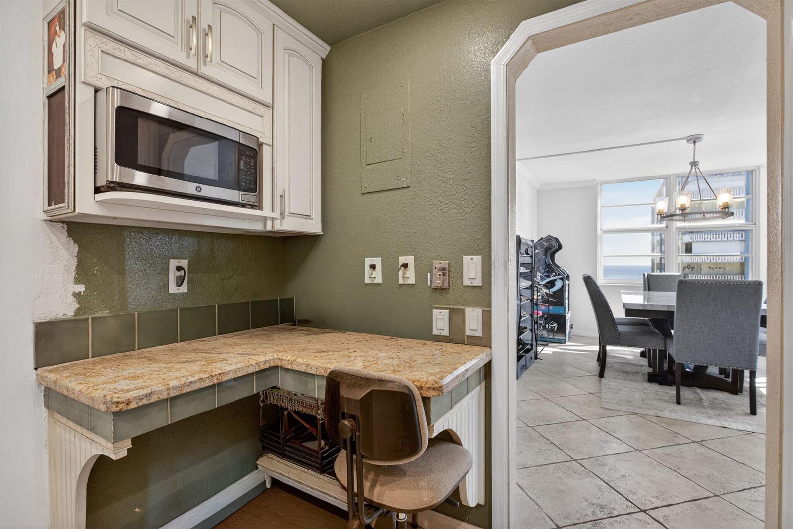 A small kitchen nook with granite countertops, white cabinets, and a view into the dining room — 301 N Ocean Boulevard # 1006, Pompano Beach FL 33062, POMPANO BEACH, FL