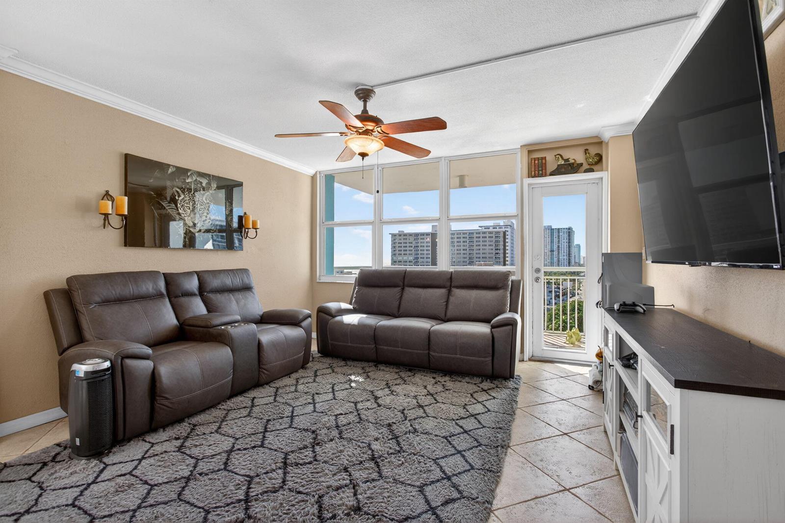 A living room features two brown leather sofas, a grey area rug, and a balcony view — 301 N Ocean Boulevard # 1006, Pompano Beach FL 33062, POMPANO BEACH, FL