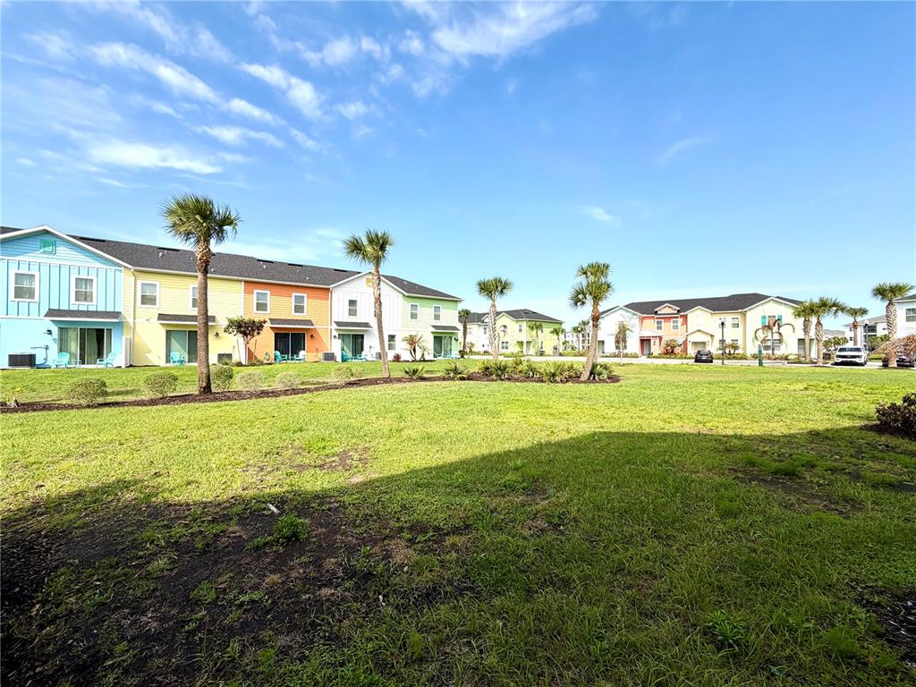 A grassy lawn sits in front of several colorful multi-story townhomes under a blue sky — 3008 CARIBBEAN SOUL DRIVE, KISSIMMEE, FL
