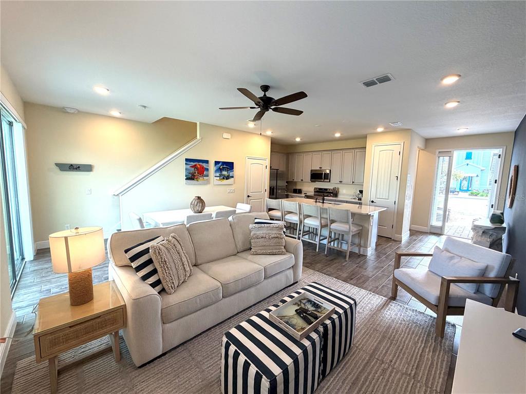 An open-concept living room and kitchen featuring a beige sofa, striped ottoman, and tile flooring — 3008 CARIBBEAN SOUL DRIVE, KISSIMMEE, FL