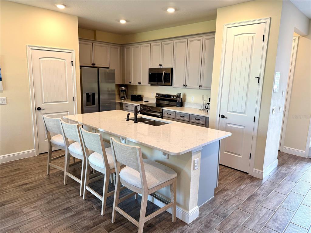 A kitchen features a large quartz-topped island with four chairs, light cabinetry, and stainless appliances — 3008 CARIBBEAN SOUL DRIVE, KISSIMMEE, FL