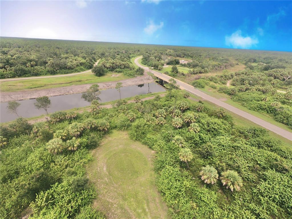 An aerial view shows a canal, a bridge, and a grassy clearing surrounded by trees — SNOWBANK COURT, NORTH PORT, FL