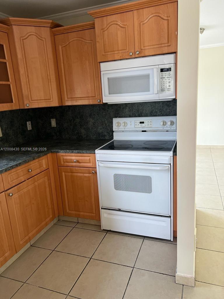 A kitchen features wood cabinets, dark countertops, and white appliances including a range and microwave — NORTH MIAMI, FL