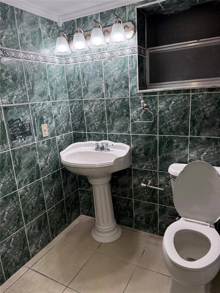 A bathroom features green marble-patterned wall tiles, a pedestal sink, and a white toilet — NORTH MIAMI, FL