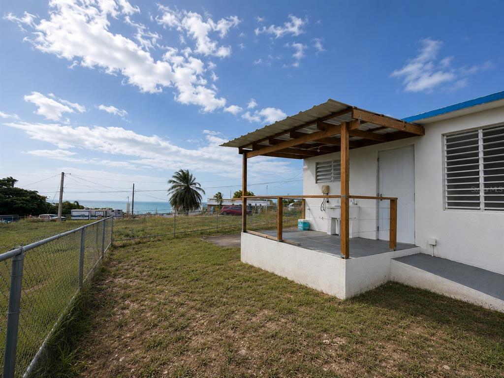 A white house features a covered porch with a wooden frame overlooking a grassy yard — CALLE PASCUA URB. MANUEL CORCHADO, ISABELA, PR