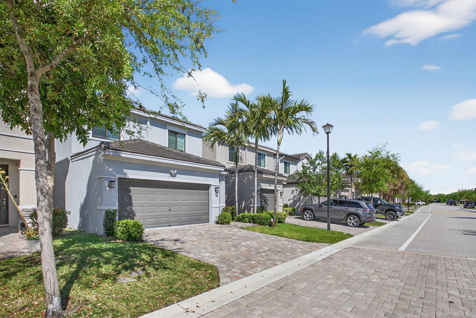 A row of two-story townhouses with gray stucco exteriors, paved driveways, and palm trees — 325 NW 33rd Lane, Pompano Beach FL 33069, POMPANO BEACH, FL