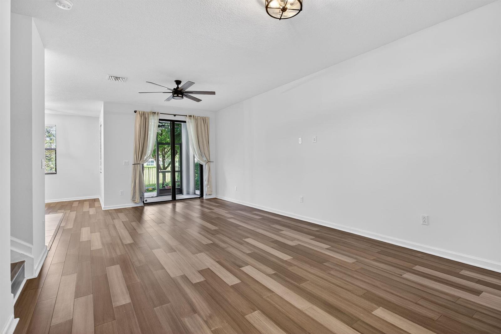 An empty living room features wood-look flooring, a ceiling fan, and sliding glass patio doors — 325 NW 33rd Lane, Pompano Beach FL 33069, POMPANO BEACH, FL