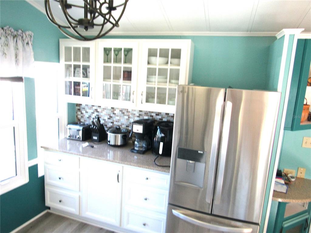 A kitchen features white cabinets with glass doors, a mosaic backsplash, and a stainless refrigerator — 9000 US HWY 192 UNIT 600, CLERMONT, FL