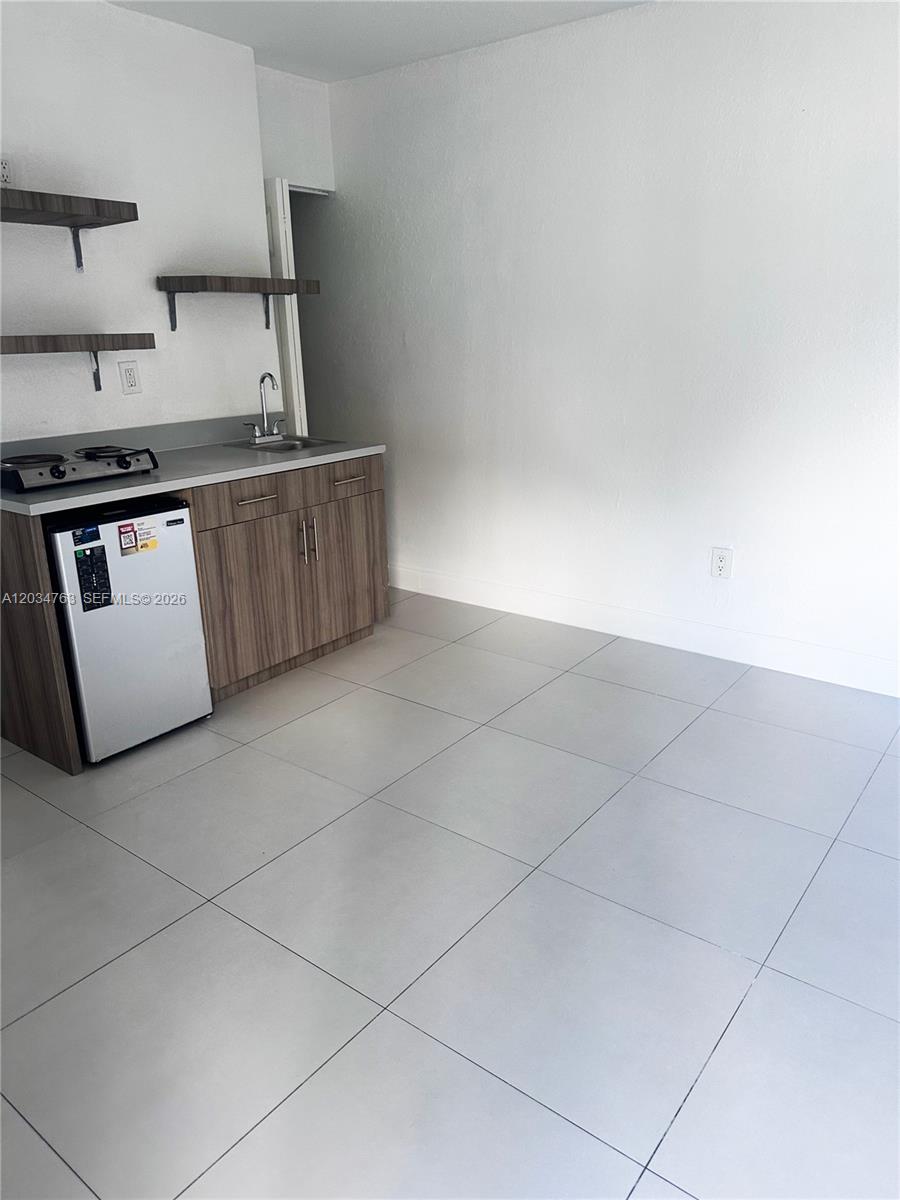A small kitchenette features a mini-fridge, sink, stovetop, and open shelving against a white wall — 1265 SW 6th St # 13, Miami FL 33135, MIAMI, FL