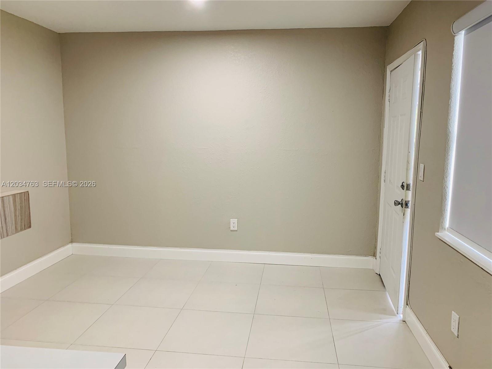 An empty room features beige walls, white tile flooring, a white door, and a window — 1265 SW 6th St # 13, Miami FL 33135, MIAMI, FL