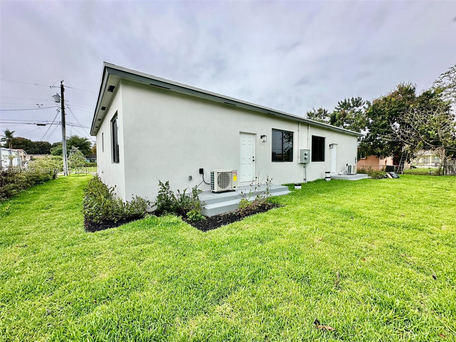 The exterior of a white, single-story house features two doors, windows, and air conditioning units — 2377 NW 105th St # 1, Miami FL 33147, MIAMI, FL