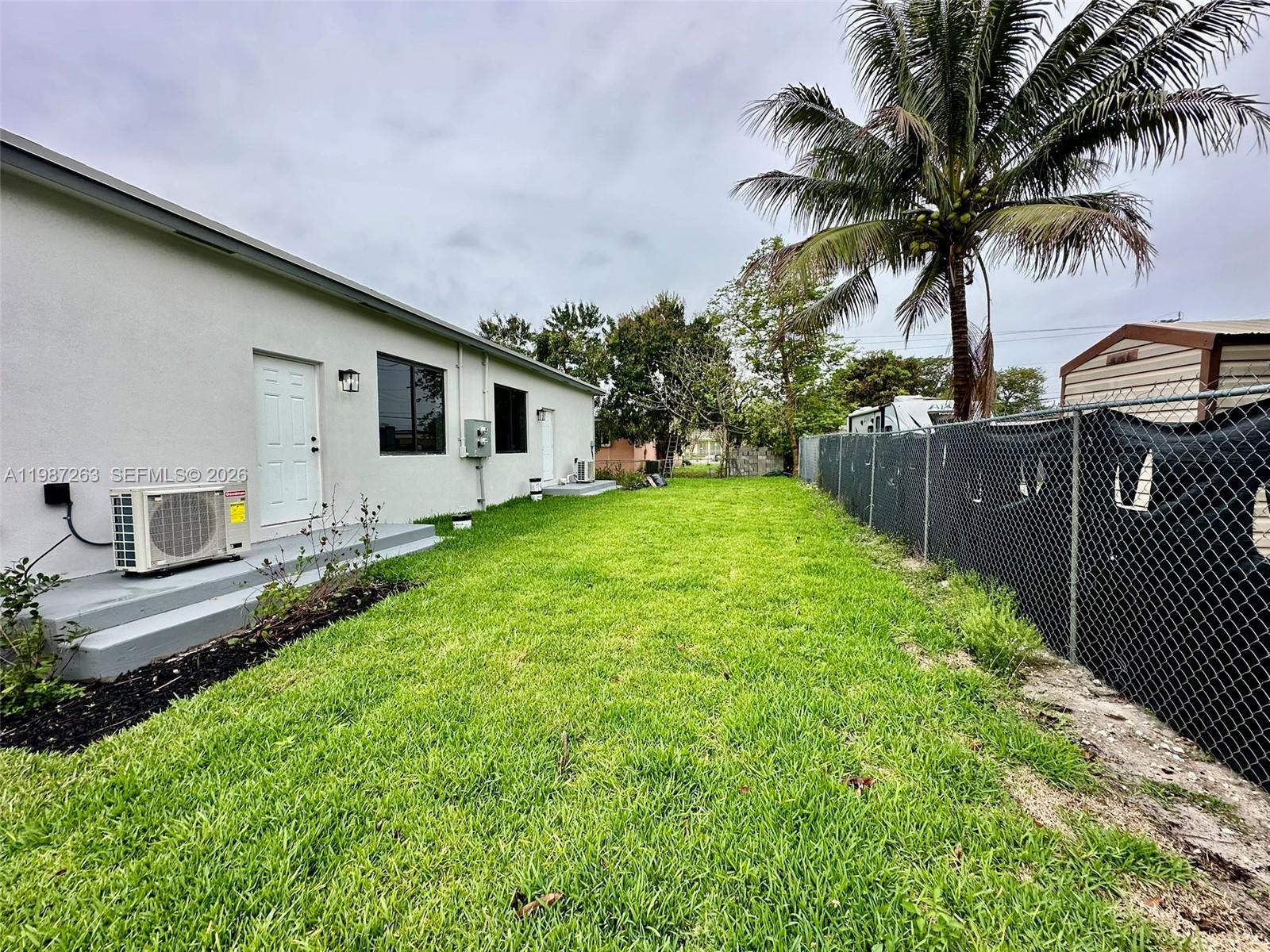 A side yard features a grassy lawn, a white exterior wall, and a chain-link fence — 2377 NW 105th St # 1, Miami FL 33147, MIAMI, FL
