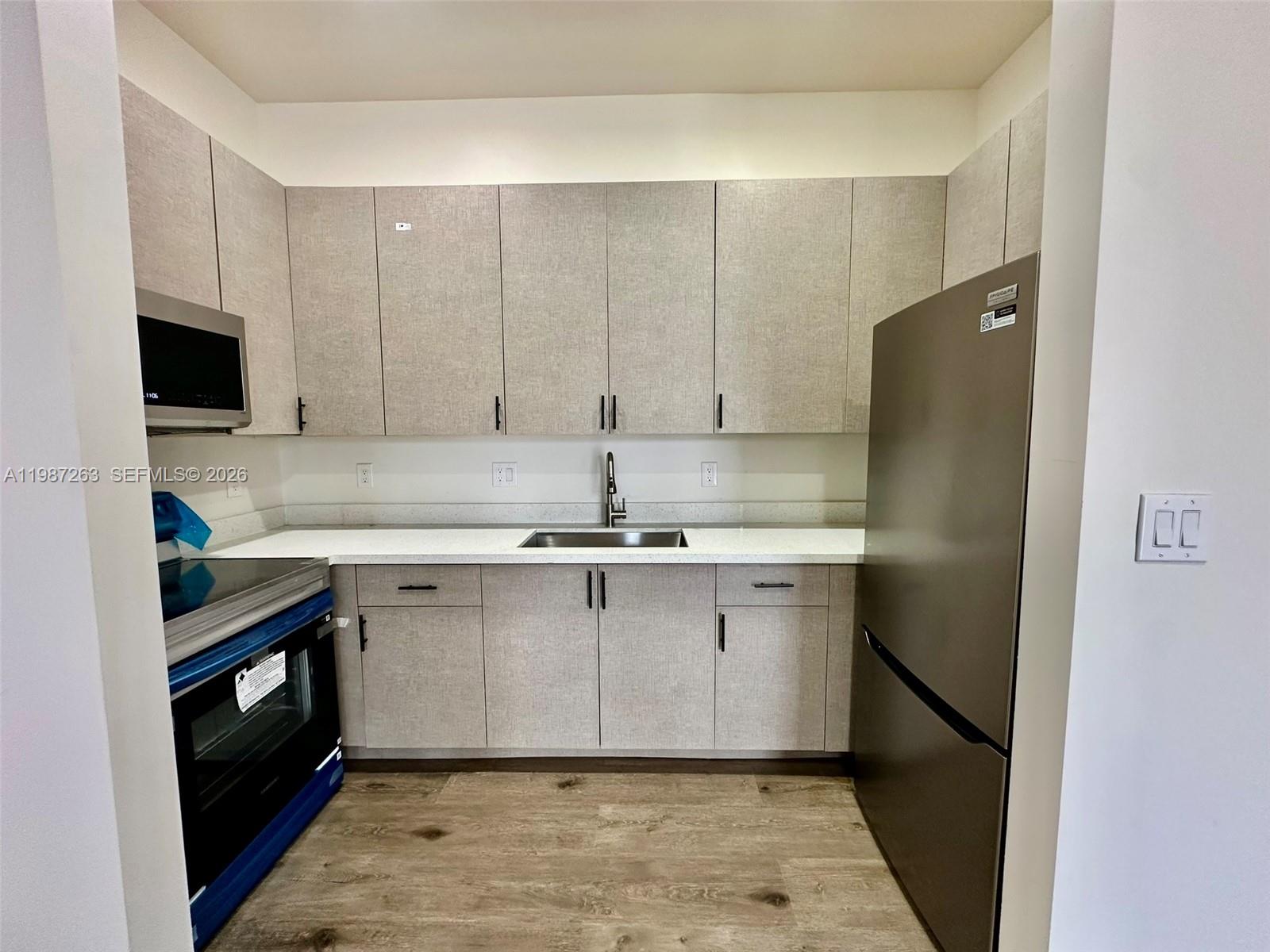A kitchen features light wood-grain cabinets, white countertops, stainless steel appliances, and wood-look flooring — 2377 NW 105th St # 1, Miami FL 33147, MIAMI, FL