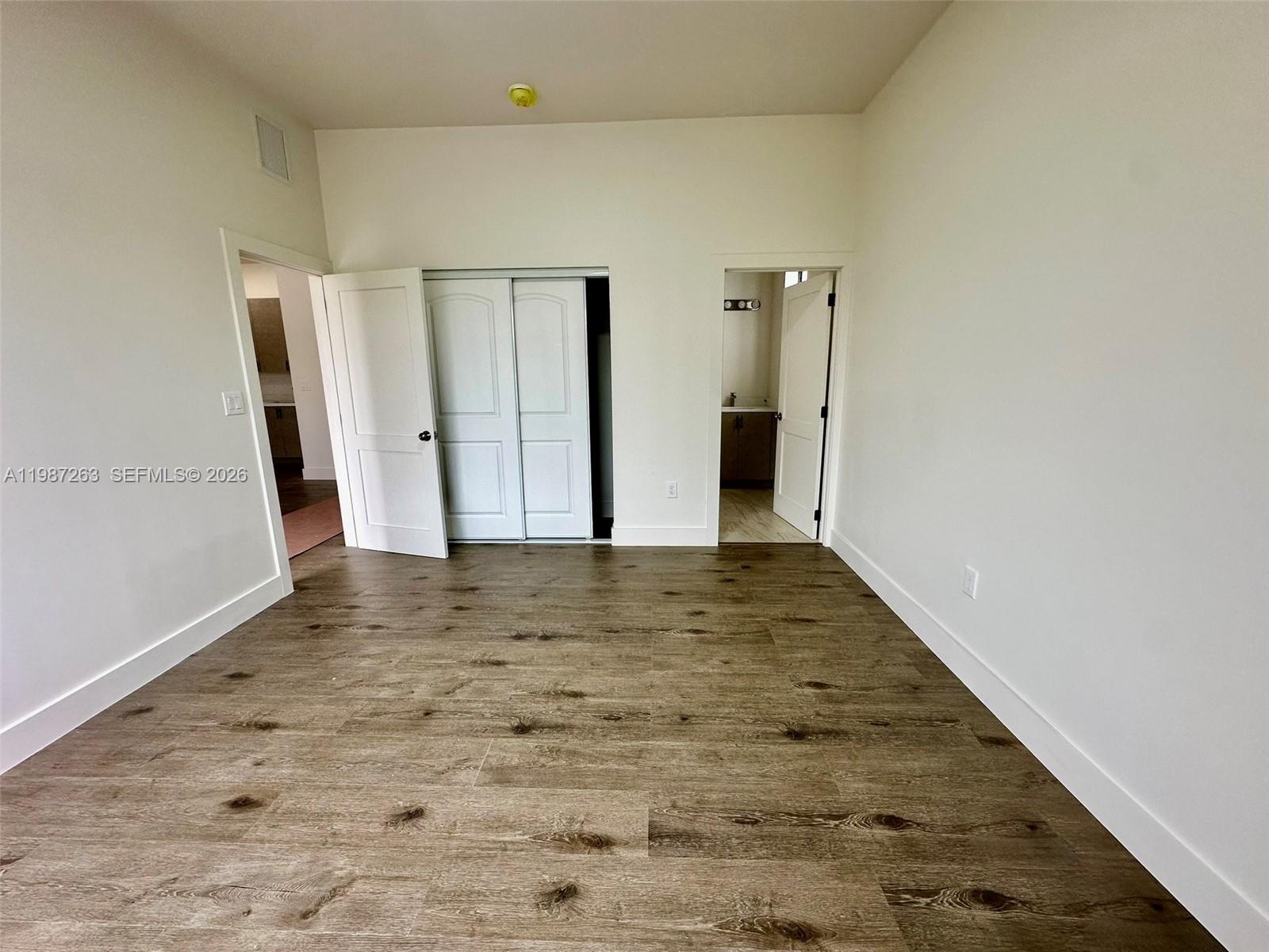 An empty room features wood-look flooring, white walls, a closet, and an attached bathroom — 2377 NW 105th St # 1, Miami FL 33147, MIAMI, FL