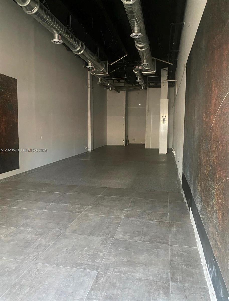 An empty commercial space features exposed ceiling ductwork, gray tiled flooring, and dark textured walls — 1427 E Alton Rd # 1427, Miami Beach FL 33139, MIAMI BEACH, FL