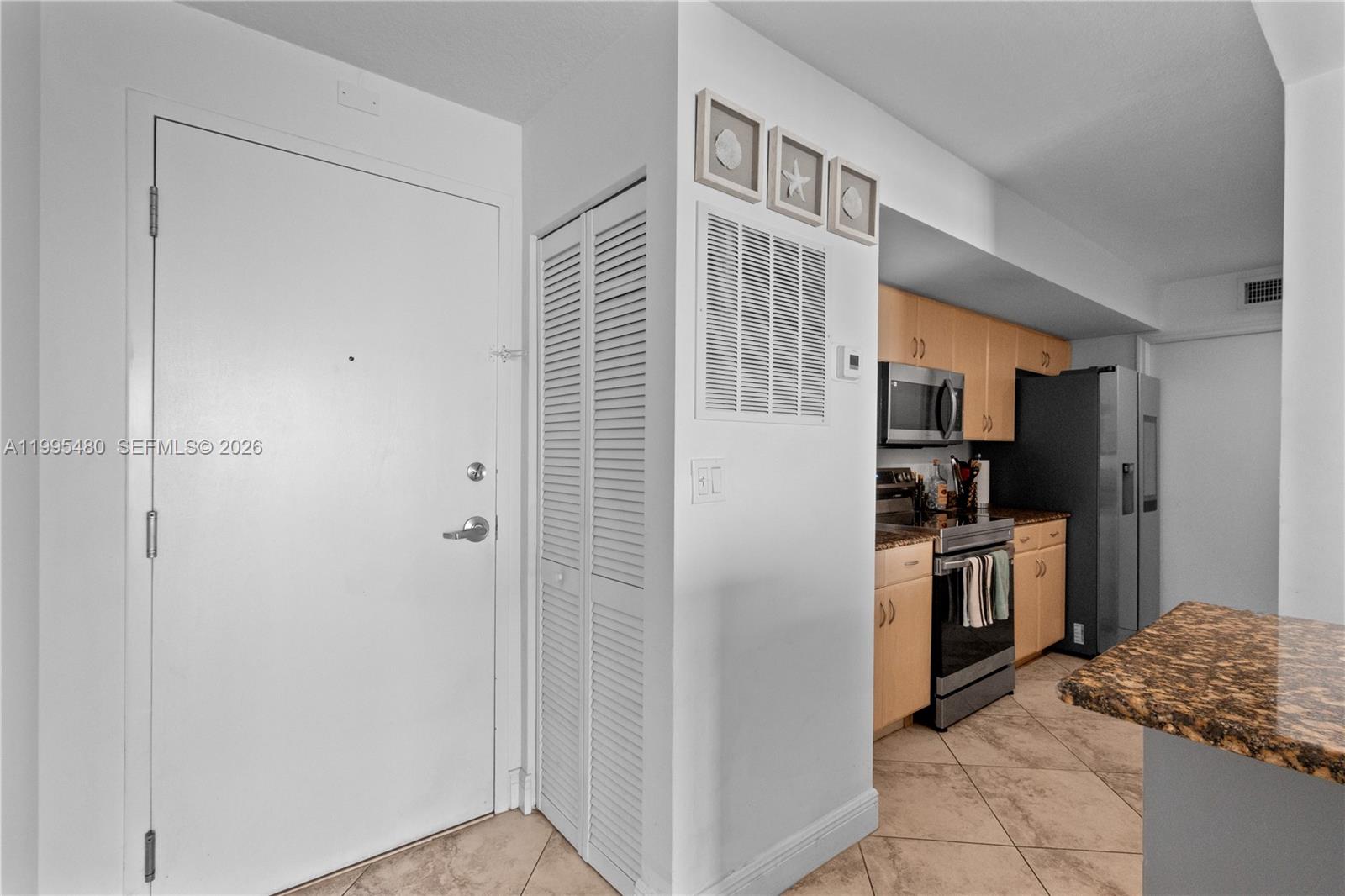 A white front door stands next to a louvered closet and an open kitchen area — 6917 Collins Ave # 1609, Miami Beach FL 33141, MIAMI BEACH, FL