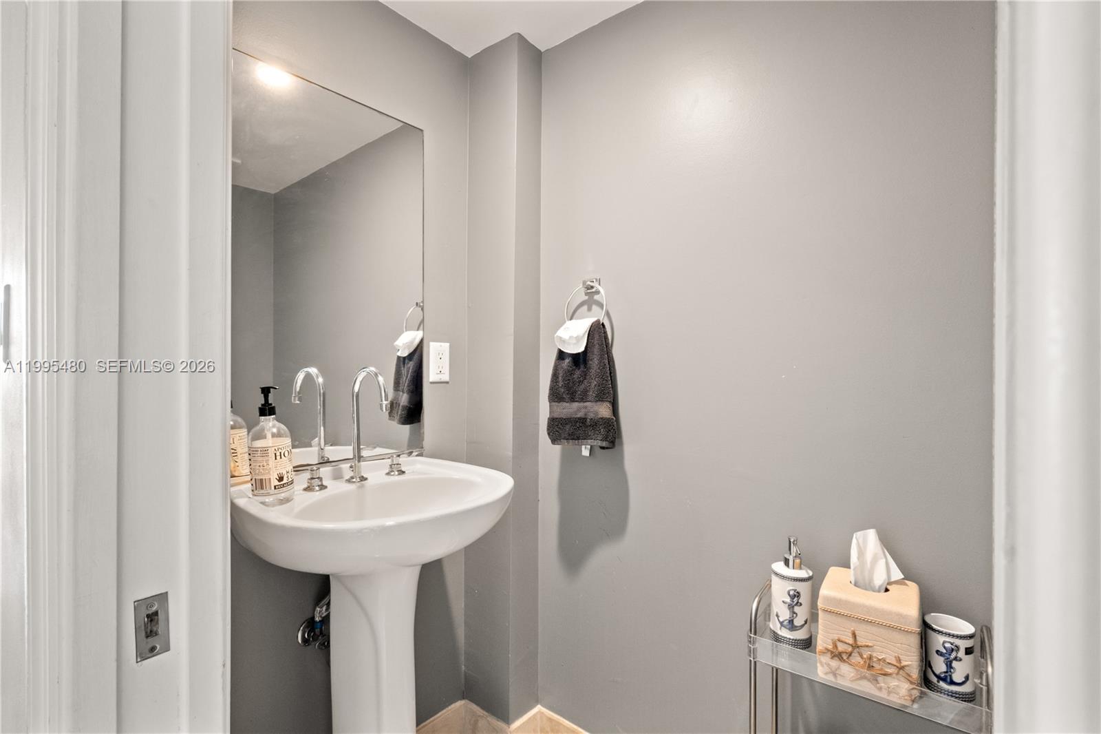A pedestal sink, a wall-mounted towel, and nautical-themed accessories are in this gray bathroom — 6917 Collins Ave # 1609, Miami Beach FL 33141, MIAMI BEACH, FL