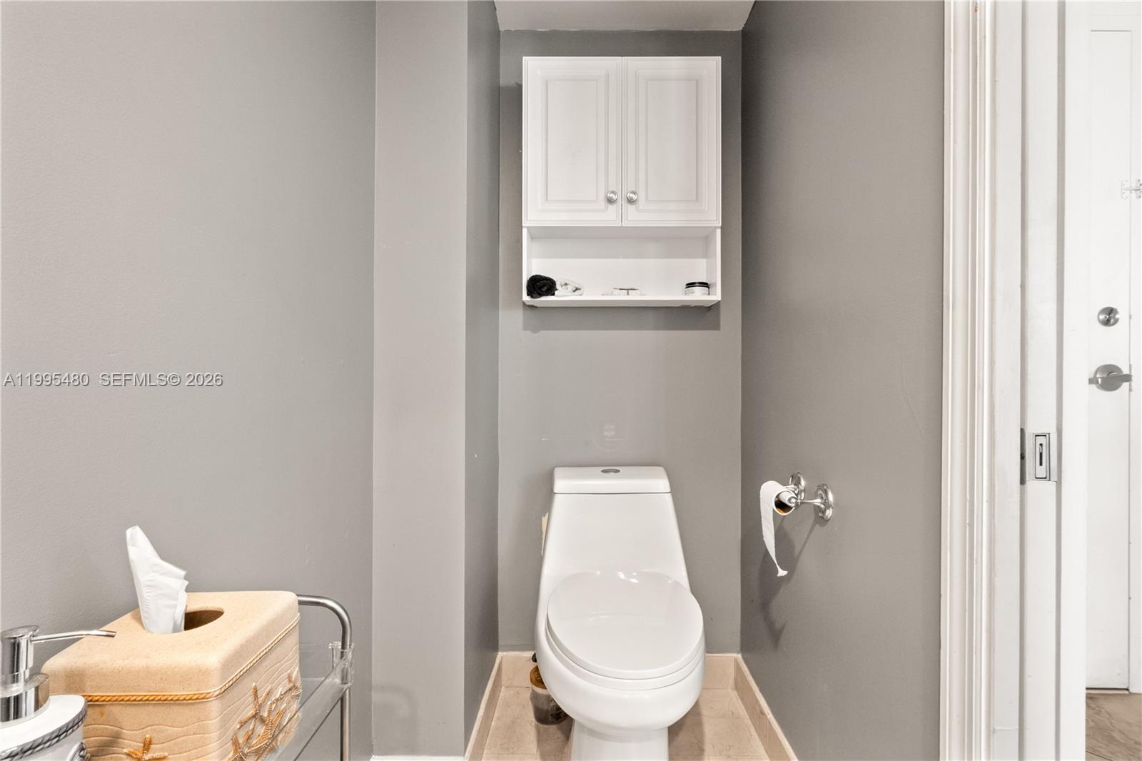 A bathroom features a white toilet, a wall-mounted cabinet, and grey walls — 6917 Collins Ave # 1609, Miami Beach FL 33141, MIAMI BEACH, FL
