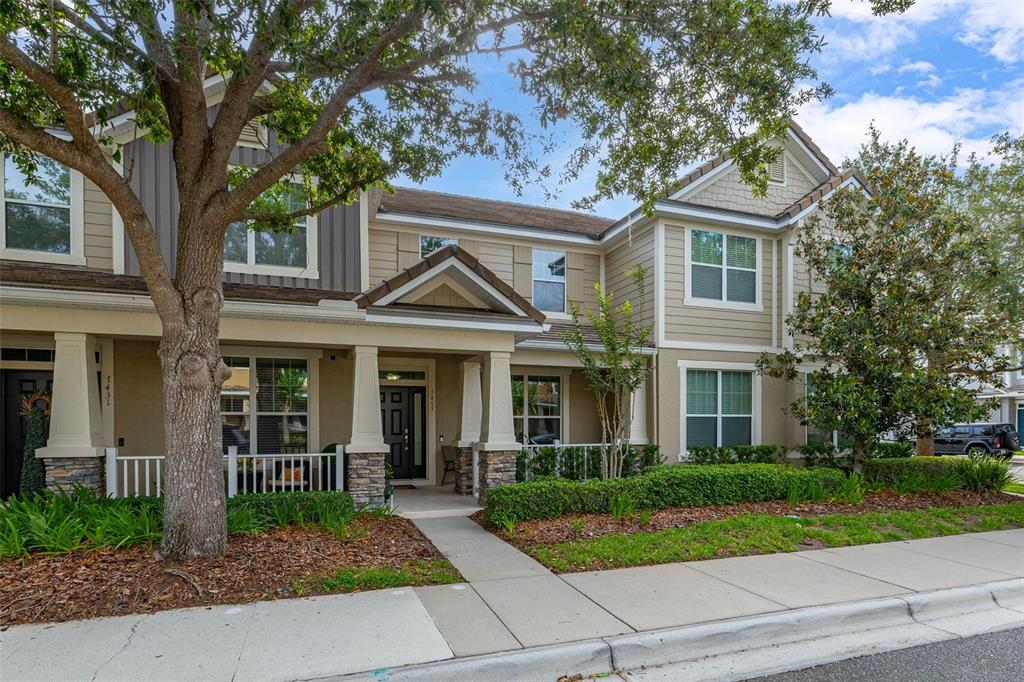 A two-story townhouse features a covered front porch, stone accents, and a landscaped yard — 7435 RIPPLEPOINTE WAY, WINDERMERE, FL