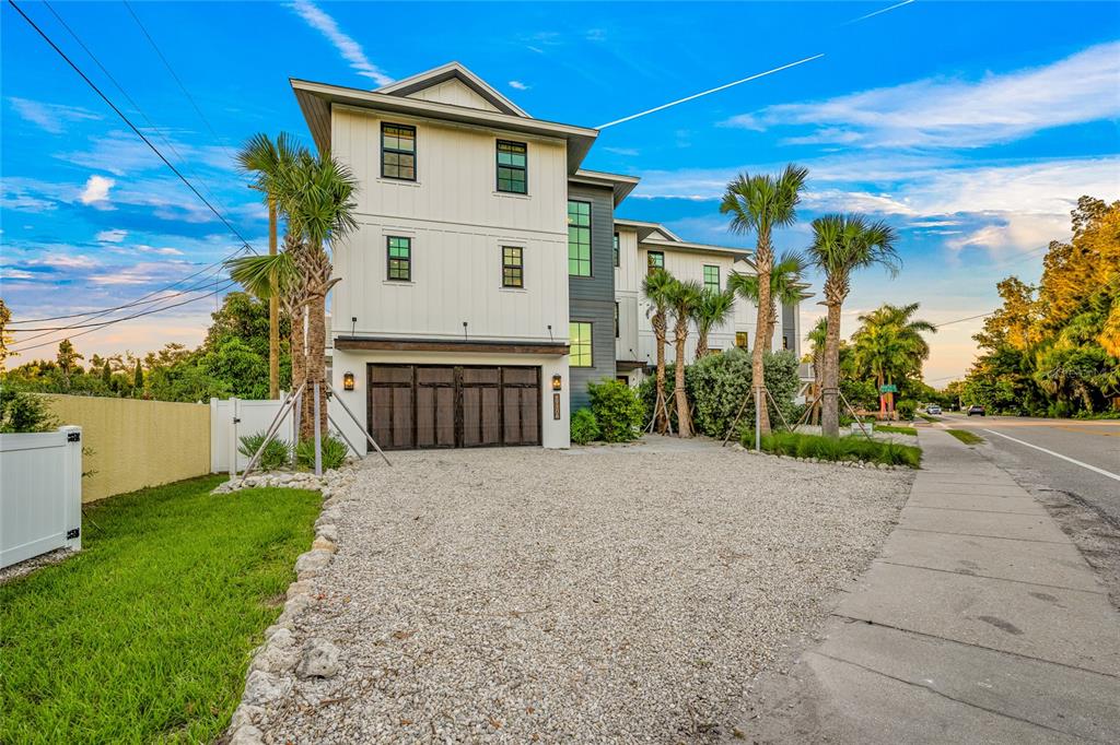 A three-story modern house with white vertical siding and a gravel driveway — 6910 MIDNIGHT PASS ROAD UNIT B, SARASOTA, FL