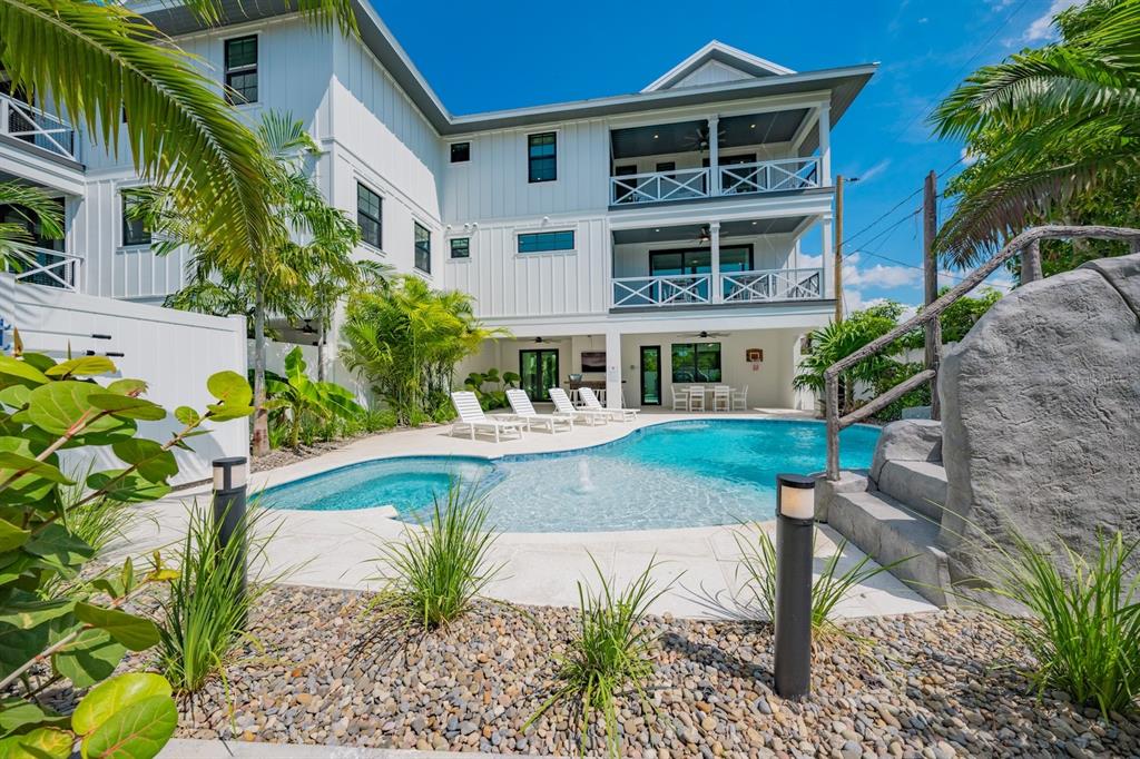 A white multi-story house features a swimming pool, lounge chairs, and a rock-themed water feature — 6910 MIDNIGHT PASS ROAD UNIT B, SARASOTA, FL