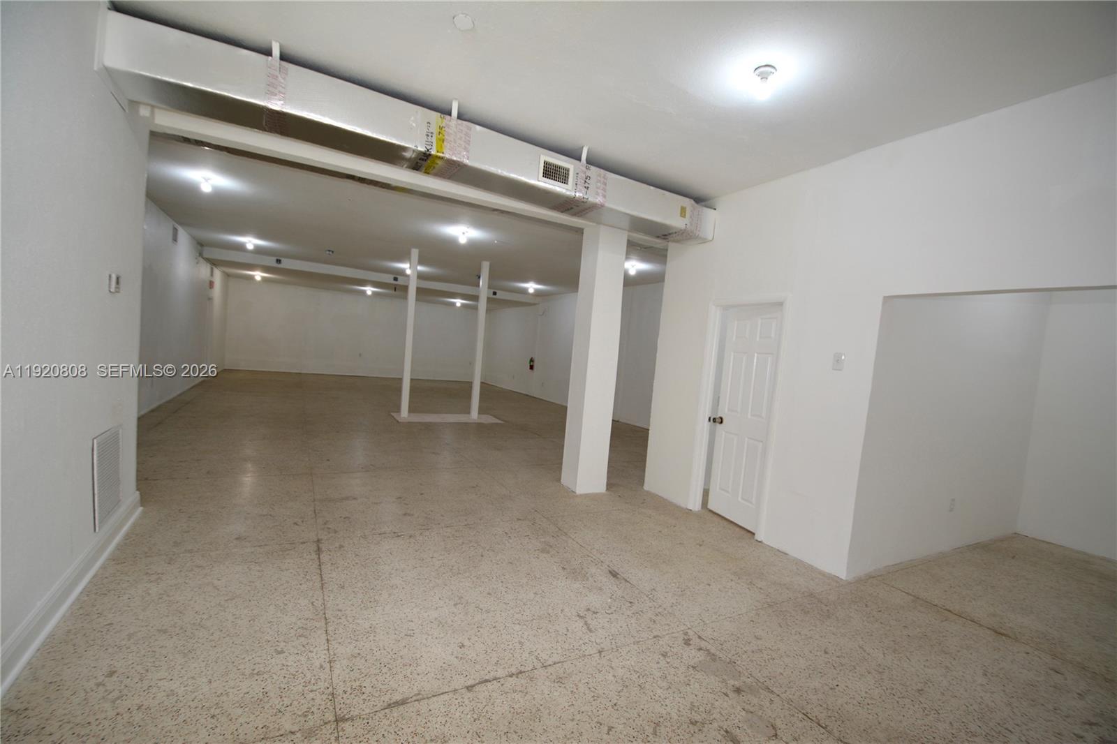 An expansive, unfinished room features white walls, a concrete floor, and exposed ceiling ductwork — 5525 NW 7th Ave, Miami FL 33127, MIAMI, FL