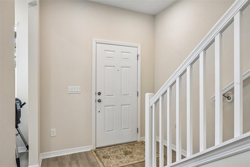 An entryway features a white front door, light-colored walls, wood-look flooring, and a white staircase — 15877 TOLLINGTON ALLEY, WINTER GARDEN, FL