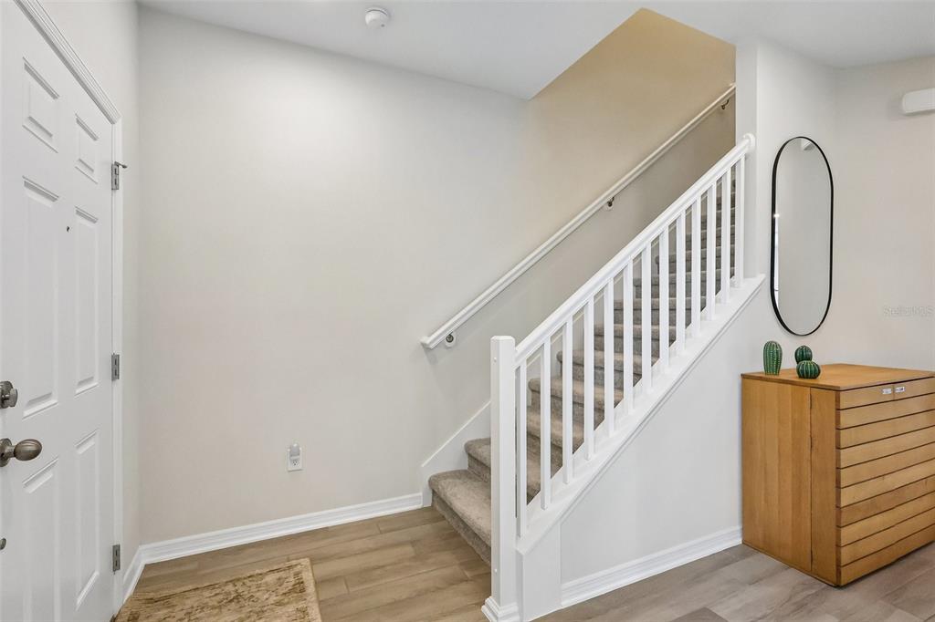 An entryway features a white door, a carpeted staircase with a white railing, and a dresser — 15877 TOLLINGTON ALLEY, WINTER GARDEN, FL