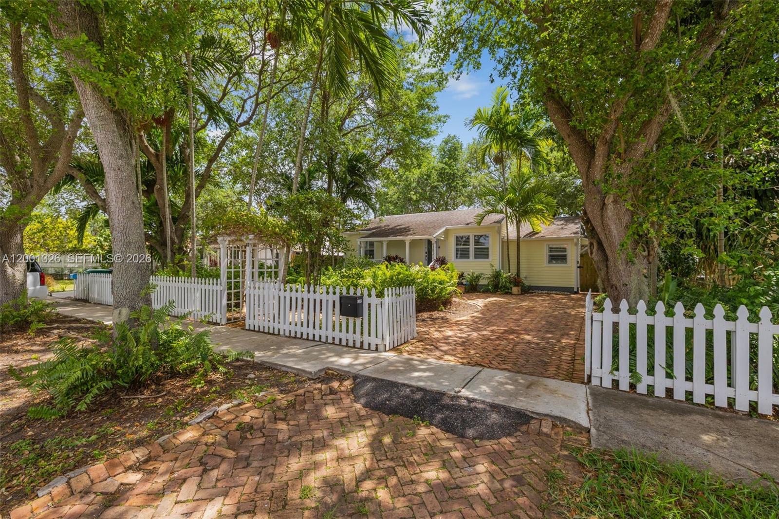 A yellow cottage with a white picket fence and a brick driveway sits among trees — 6382 SW 38th St, Miami FL 33155, MIAMI, FL