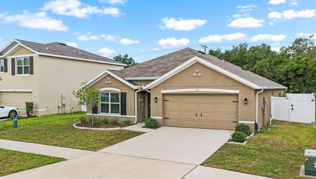 A tan, single-story house with a two-car garage and a white vinyl fence — 1911 BLUE STREAM STREET, RUSKIN, FL