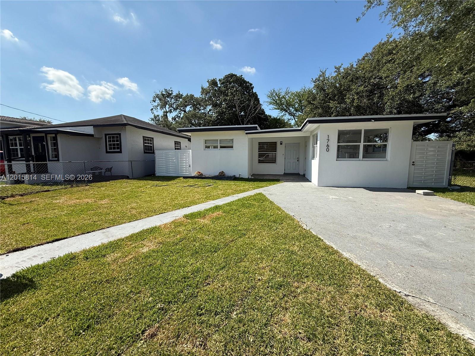 A white single-story house with a concrete driveway and a front lawn under a blue sky — 1760 NW 84th St, Miami FL 33147, MIAMI, FL