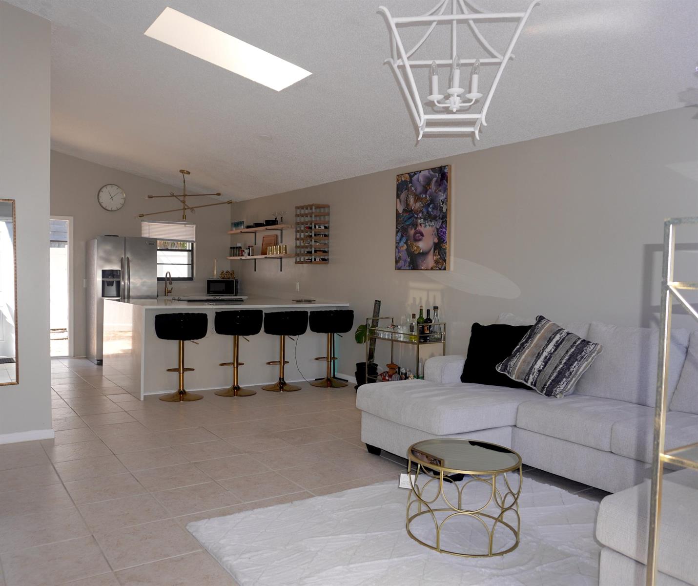 An open-concept living room and kitchen featuring a white island, bar stools, and tile flooring — 8731 Uranus Terrace, West Palm Beach FL 33403, WEST PALM BEACH, FL