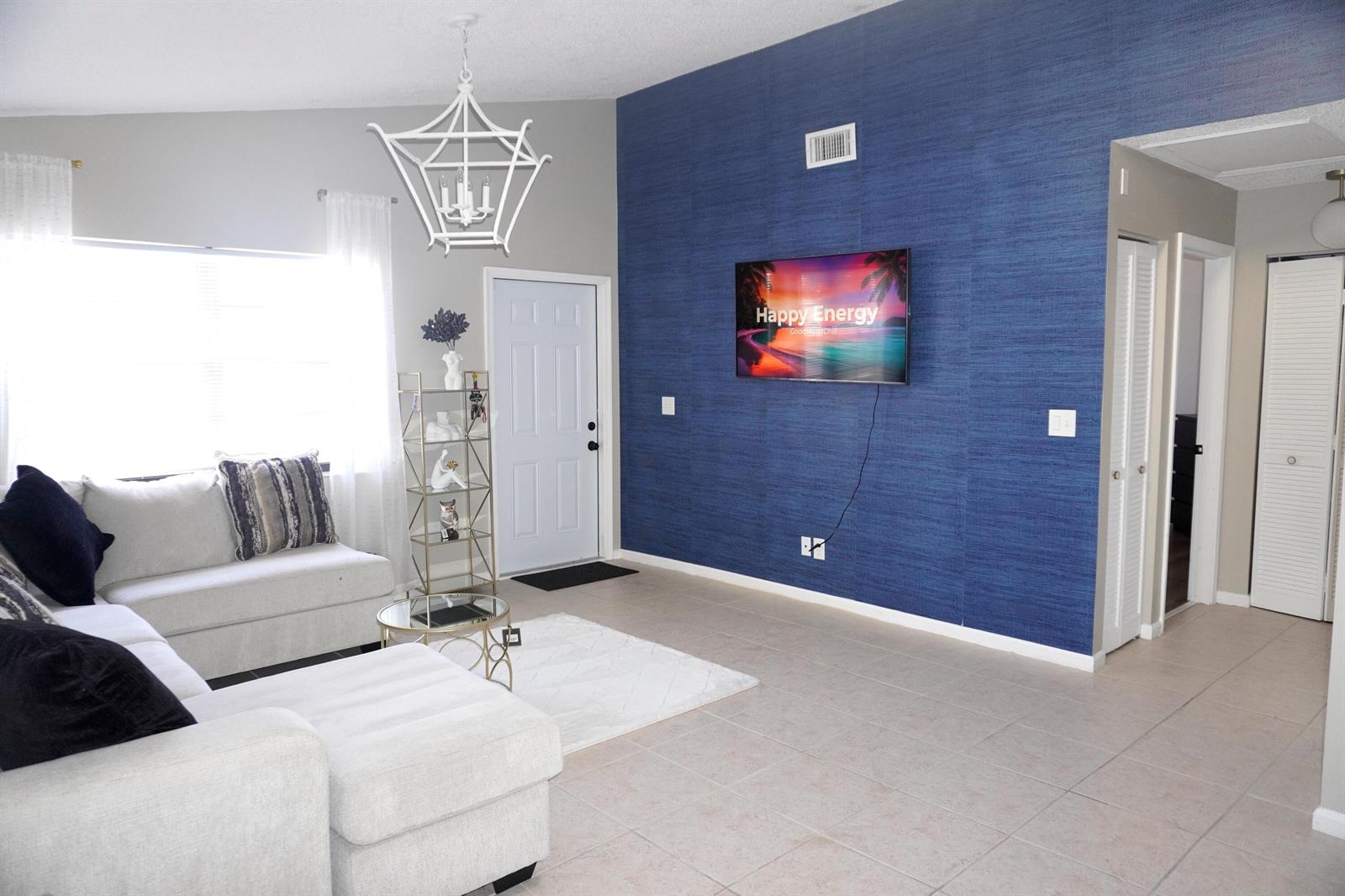 A living room features a blue textured accent wall with a mounted television and tile flooring — 8731 Uranus Terrace, West Palm Beach FL 33403, WEST PALM BEACH, FL