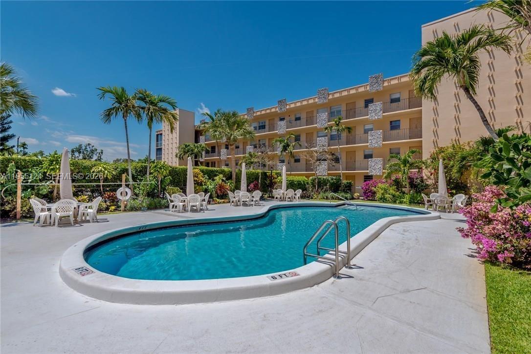 An outdoor swimming pool is surrounded by a patio with tables, chairs, and palm trees — 2145 Pierce St # 326, Hollywood FL 33020, HOLLYWOOD, FL