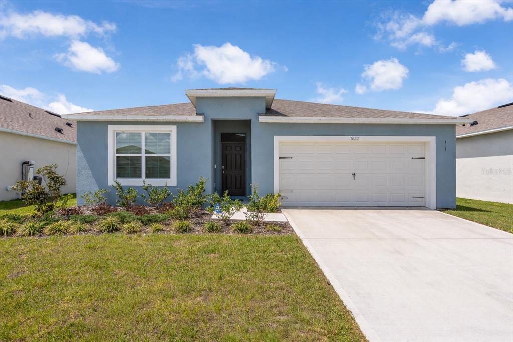A single-story blue house with a white garage door and a front lawn — 1022 TUPELO TRAIL, HAINES CITY, FL