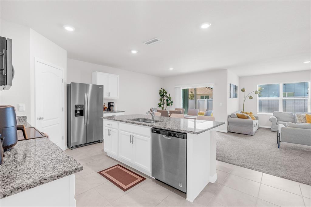 A kitchen with white cabinets and granite countertops opens into a carpeted living area — 1022 TUPELO TRAIL, HAINES CITY, FL