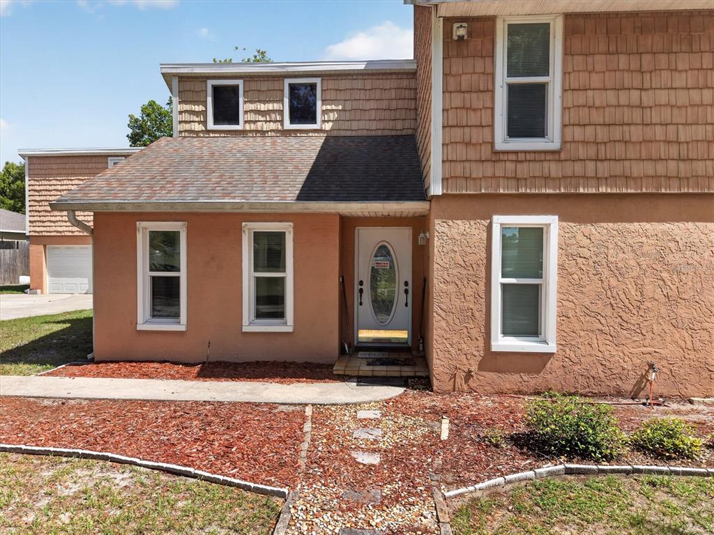 The exterior of a two-story house features tan stucco, brown shingles, and a front entrance — 1720 SUNSET VIEW CIRCLE, APOPKA, FL
