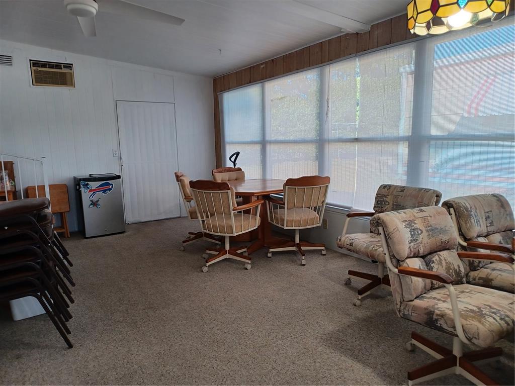 A sunroom features a dining table with chairs, carpeted flooring, and large windows with blinds — 34701 ROSEBUD ROW, ZEPHYRHILLS, FL