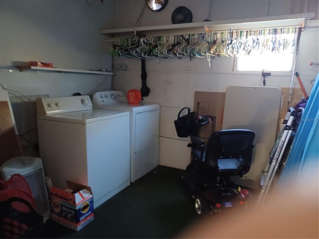 A laundry room features a white washer and dryer, a mobility scooter, and hanging clothes — 34701 ROSEBUD ROW, ZEPHYRHILLS, FL