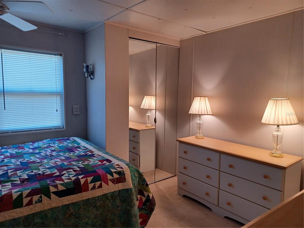 A bedroom features a bed with a colorful quilt, a dresser with lamps, and mirrored closets — 34701 ROSEBUD ROW, ZEPHYRHILLS, FL