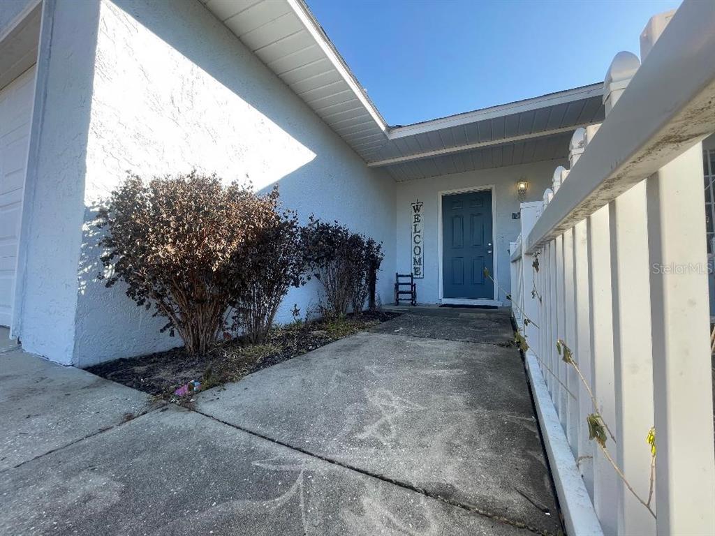 A concrete walkway leads to a blue front door with a welcome sign — 36422 BIRDIE COURT, GRAND ISLAND, FL
